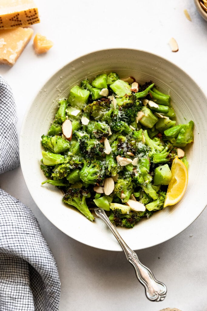 Bowl of broccoli with sliced almonds and lemon wedge.