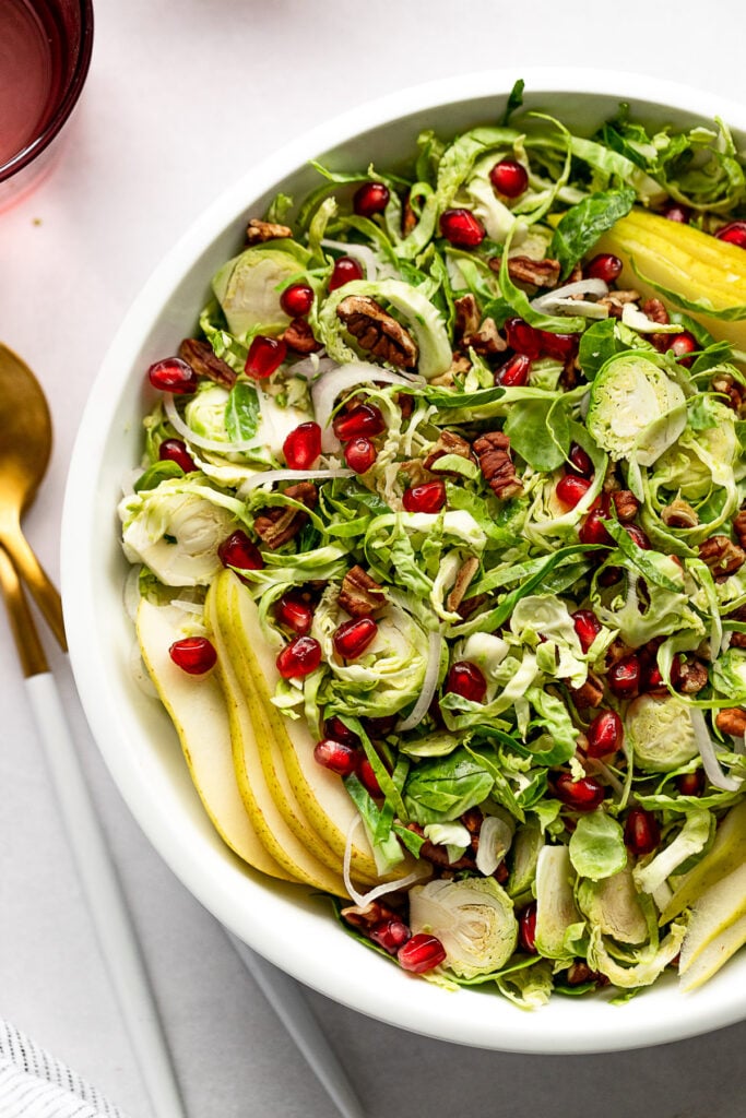 Up close bowl of shredded brussels salad with pomegranate seeds, pear slices.
