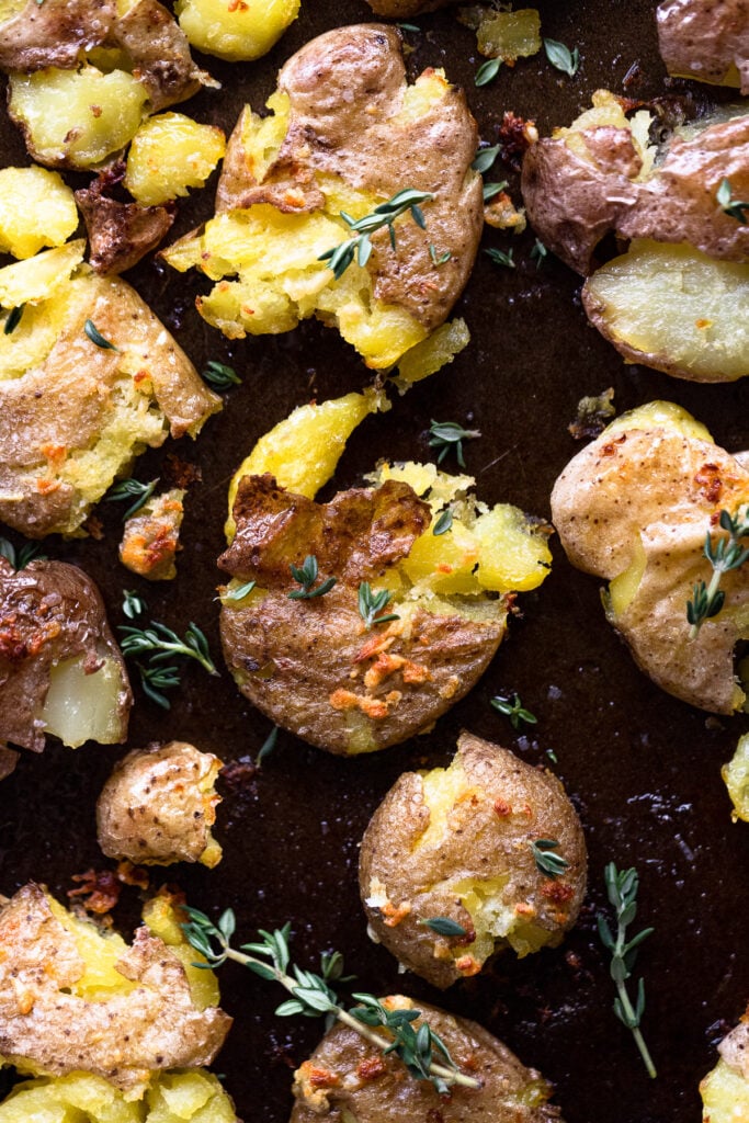 Smashed potatoes on pan with thyme leaves.