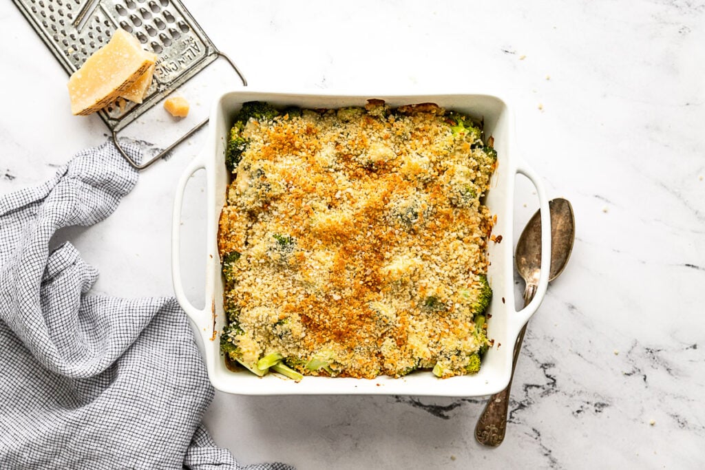 Baked broccoli au gratin next to spoon and parmesan cheese.