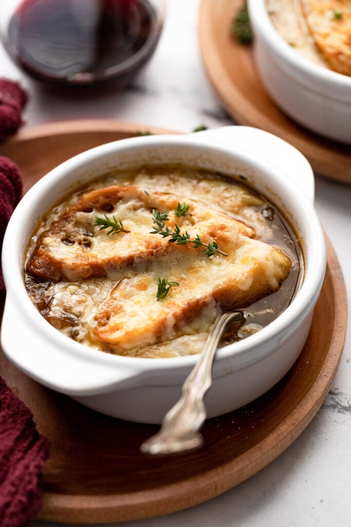 Bowl of french onion soup with bread and cheese on top on plate with spoon.