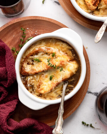 Overhead view of bowl of french onion soup on plate with spoon, linen and wine glass.