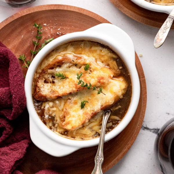 Overhead view of bowl of french onion soup on plate with spoon, linen and wine glass.
