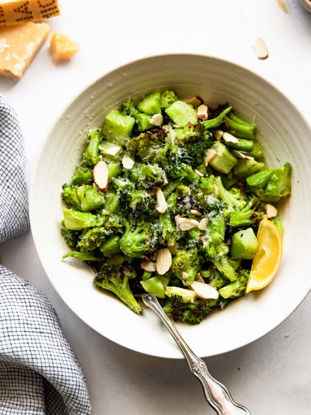 Bowl of broccoli with sliced almonds and lemon wedge.