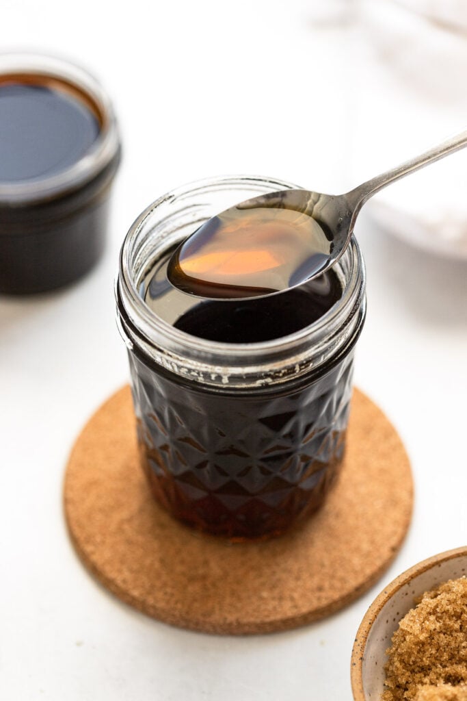 Spoon scooping brown sugar simple syrup from jar.