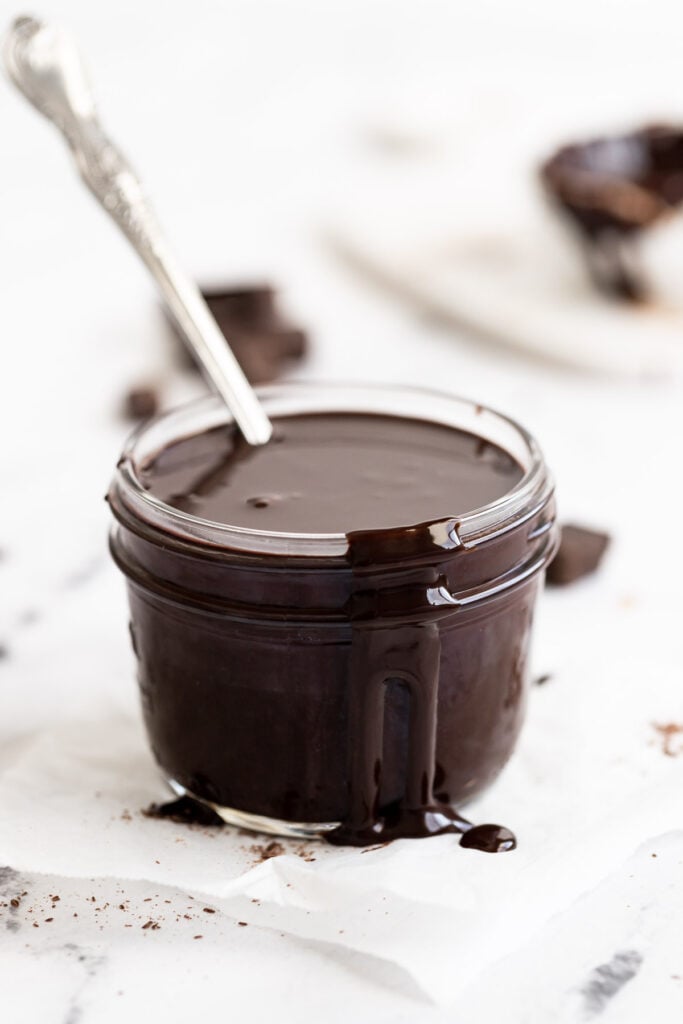 Chocolate syrup in jar with spoon and dripping over edge.