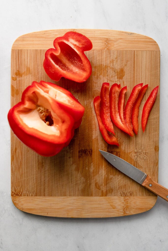 Red bell pepper on cutting board with sticks of pepper cut.