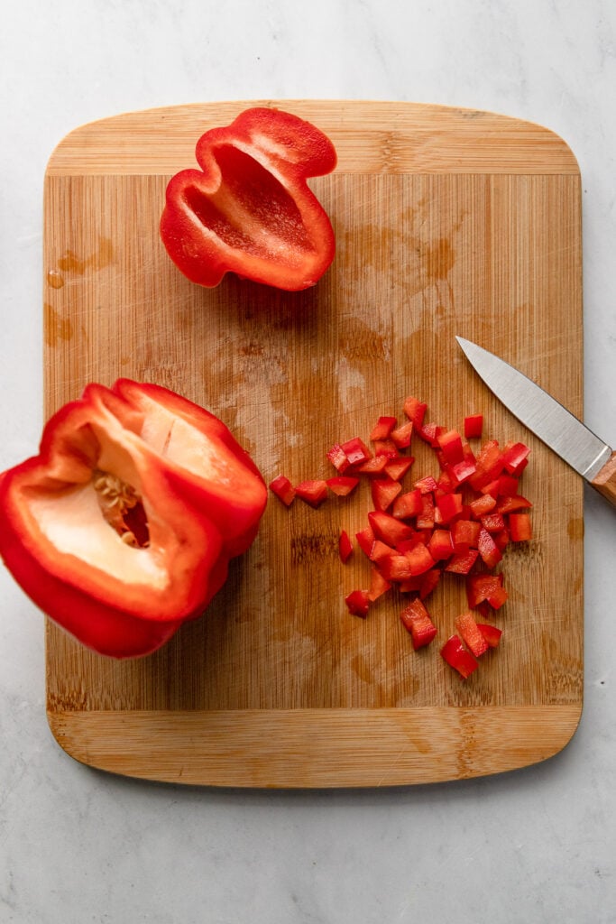 Red bell pepper on cutting board with one section diced.