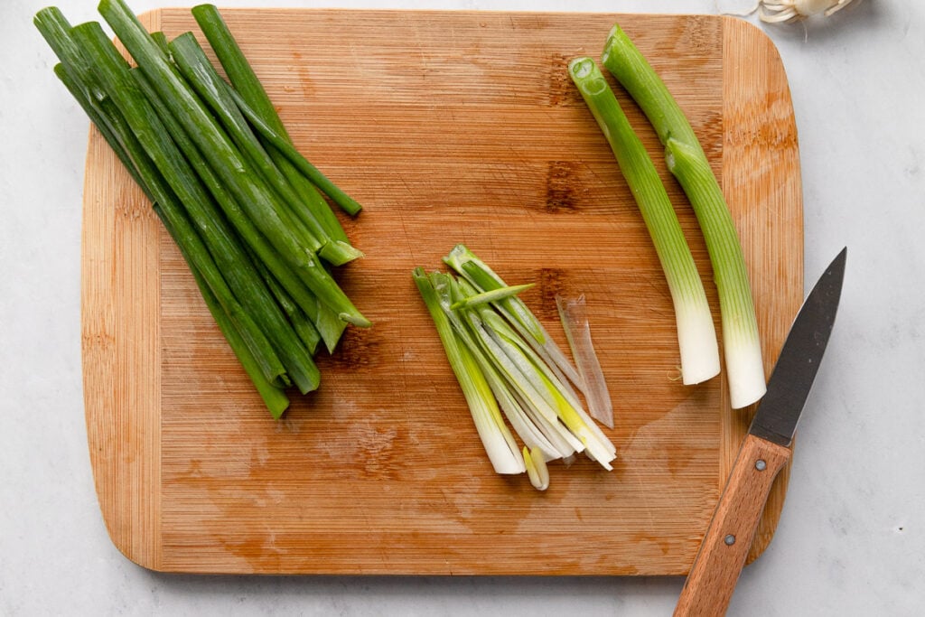 Green onions on cutting board with green parts cut off, and white and light green parts whole and sliced.