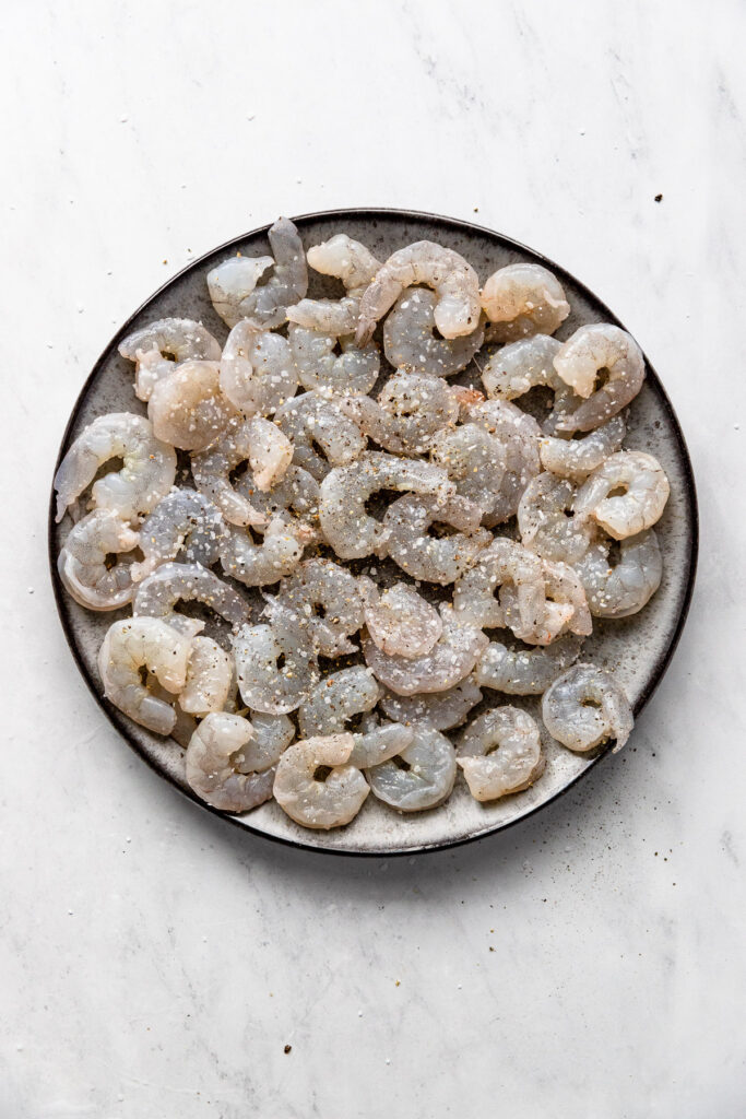 Plate of raw shrimp with salt and pepper.
