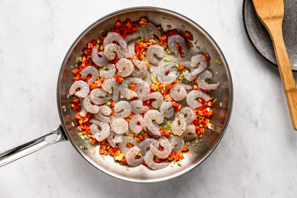 Raw shrimp added to skillet with red bell pepper and scallion.