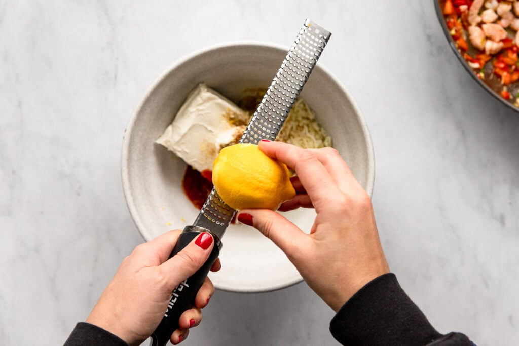 Hand using microplane to zest lemon over bowl.