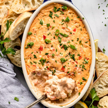 Baker of shrimp dip with spoon scooping next to baguette slices.