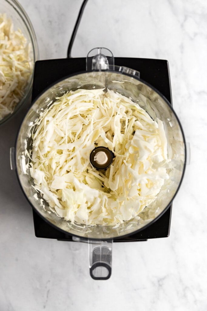 Sliced cabbage in food processor bowl.