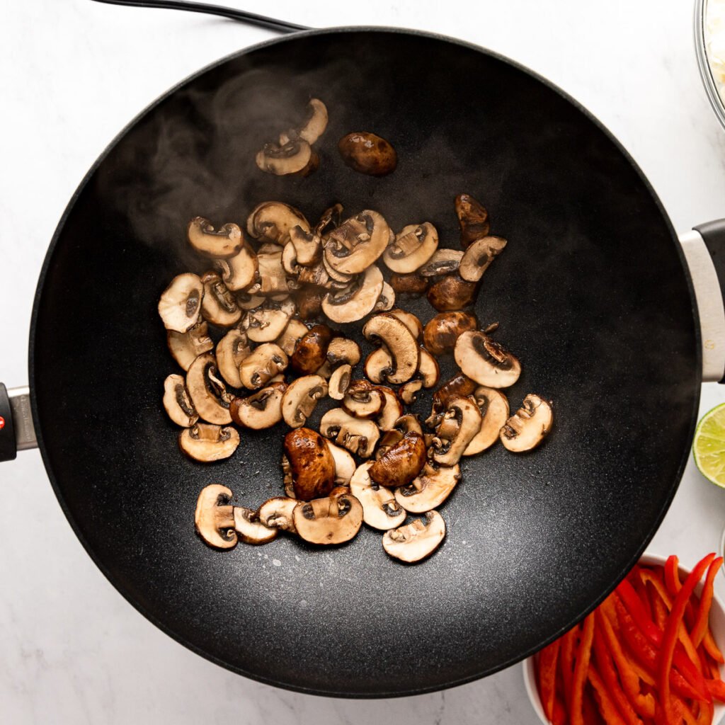 Wok with cooked sliced mushrooms.