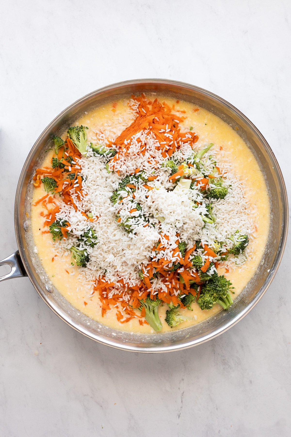 Skillet with cheese sauce and added broccoli, rice, and carrots.