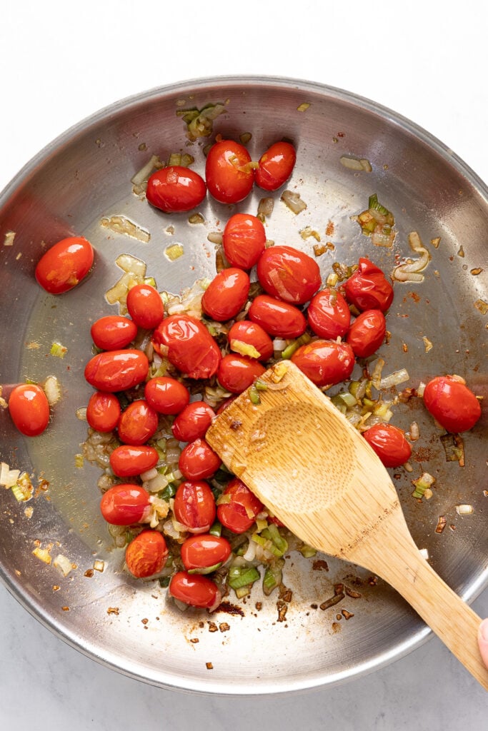 Spoon smashing tomatoes in skillet.