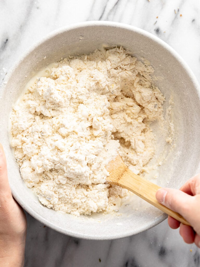 Hand stirring dough with wooden spoon.