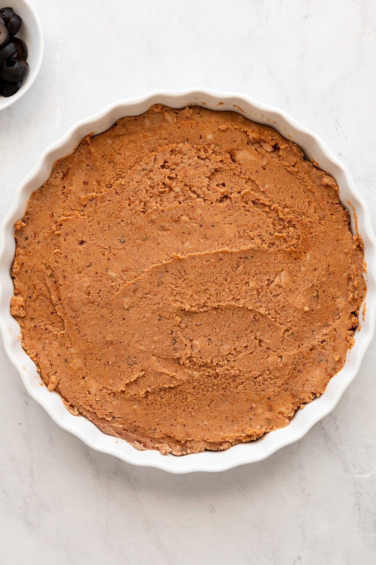 Tart pan with refried beans spread on bottom.