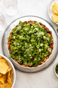 Overhead look at taco dip with shredded lettuce next to bowl of tortilla chips.