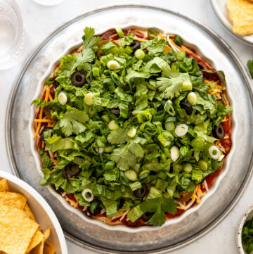 Overhead look at taco dip with shredded lettuce next to bowl of tortilla chips.