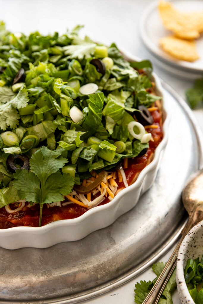 Side view of tart pan with layered taco dip next to bowl of green onions and chips.