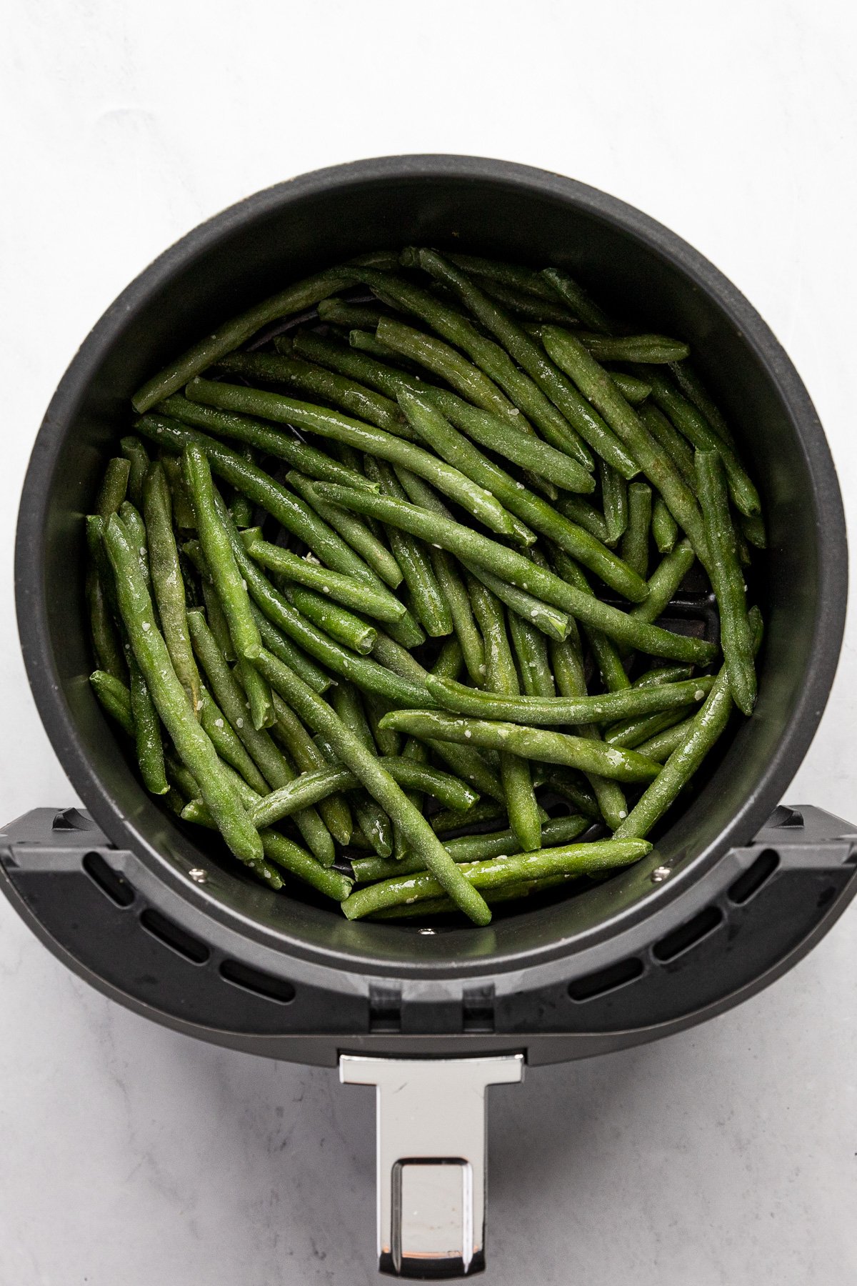Frozen green beans spread in air fryer basket.