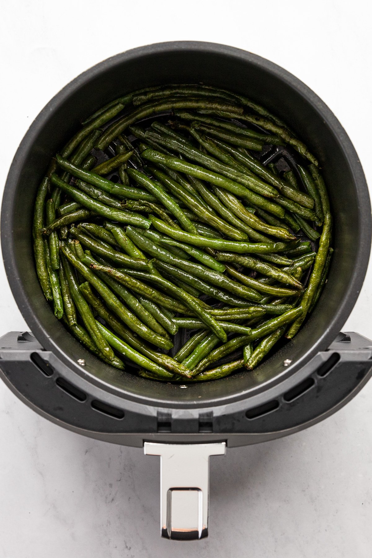 Green beans in air fryer basket after cooking.