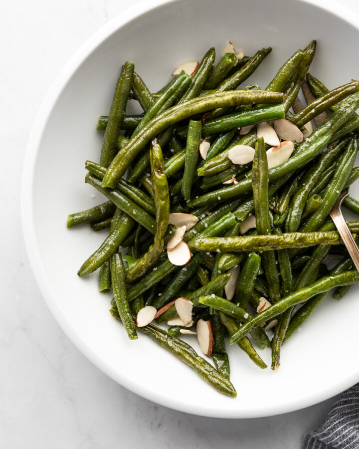 White bowl with green beans and almonds.