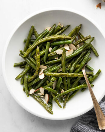 White bowl with green beans topped with sliced almonds and fork.