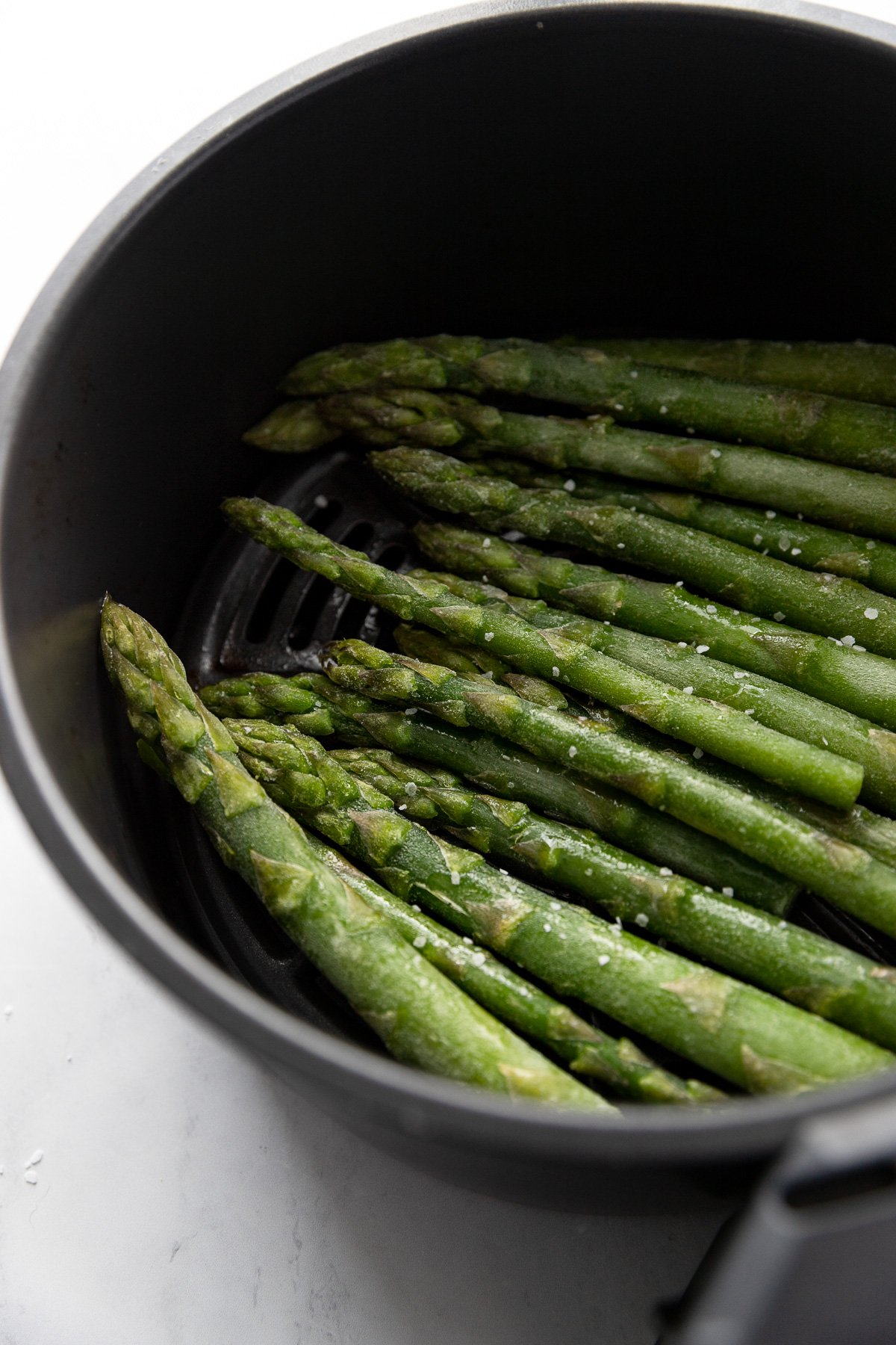 Frozen asparagus spears in basket of air fryer.