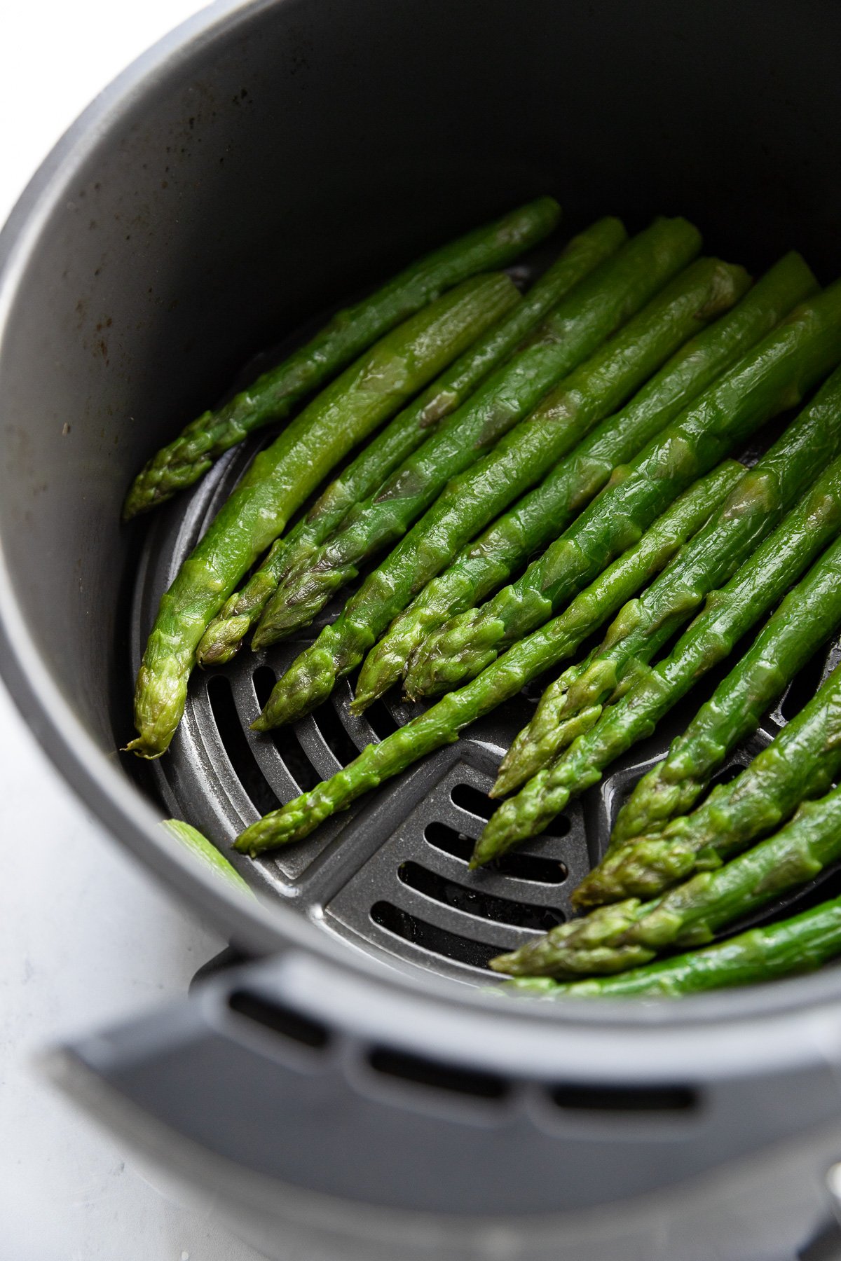 Asparagus spears in basket of air fryer after cooking.