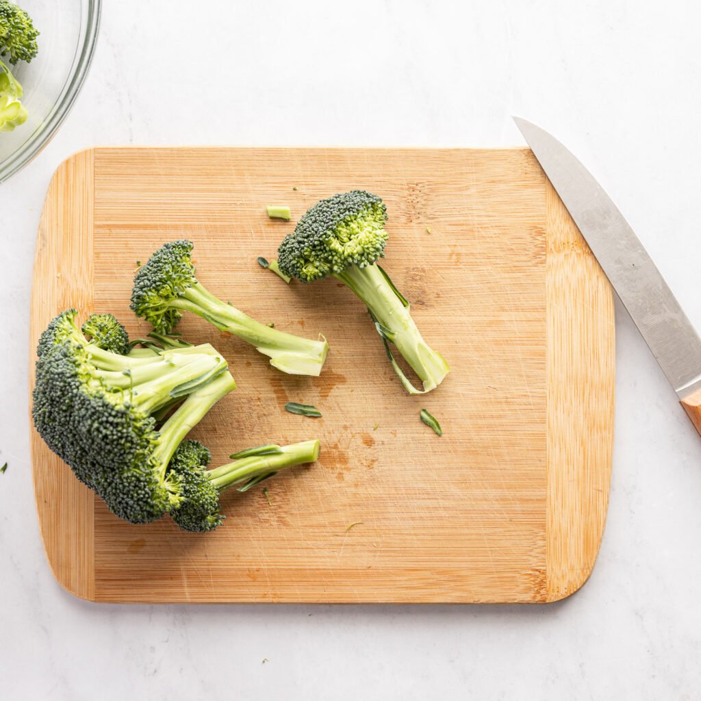 Broccoli cut on cutting board next to knife.