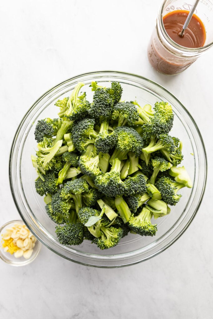 Bowl of chopped broccoli next to jar of stir fry sauce and bowl of sliced garlic and ginger.