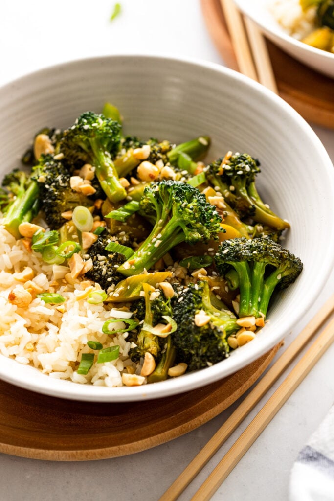 Side view of bowl of broccoli stir fry with rice, peanuts, and green onions.