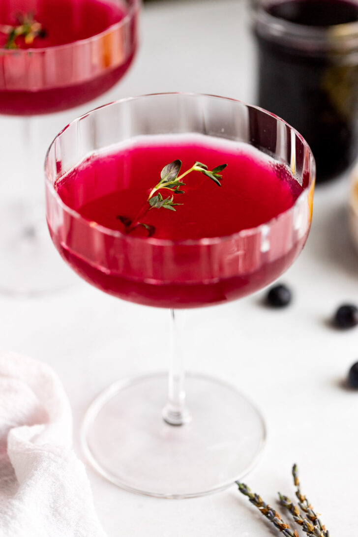 Pink drink in glass next to lavender sprigs and blueberries.