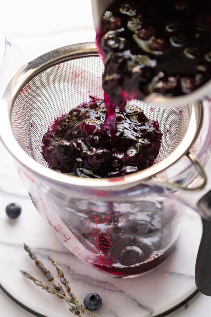 Pouring blueberry syrup into strainer.