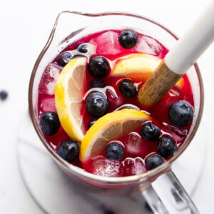 Pitcher of blueberry lemonade with lemon slices and blueberries.