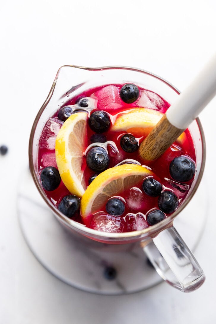 Pitcher of blueberry lemonade with lemon slices and blueberries.