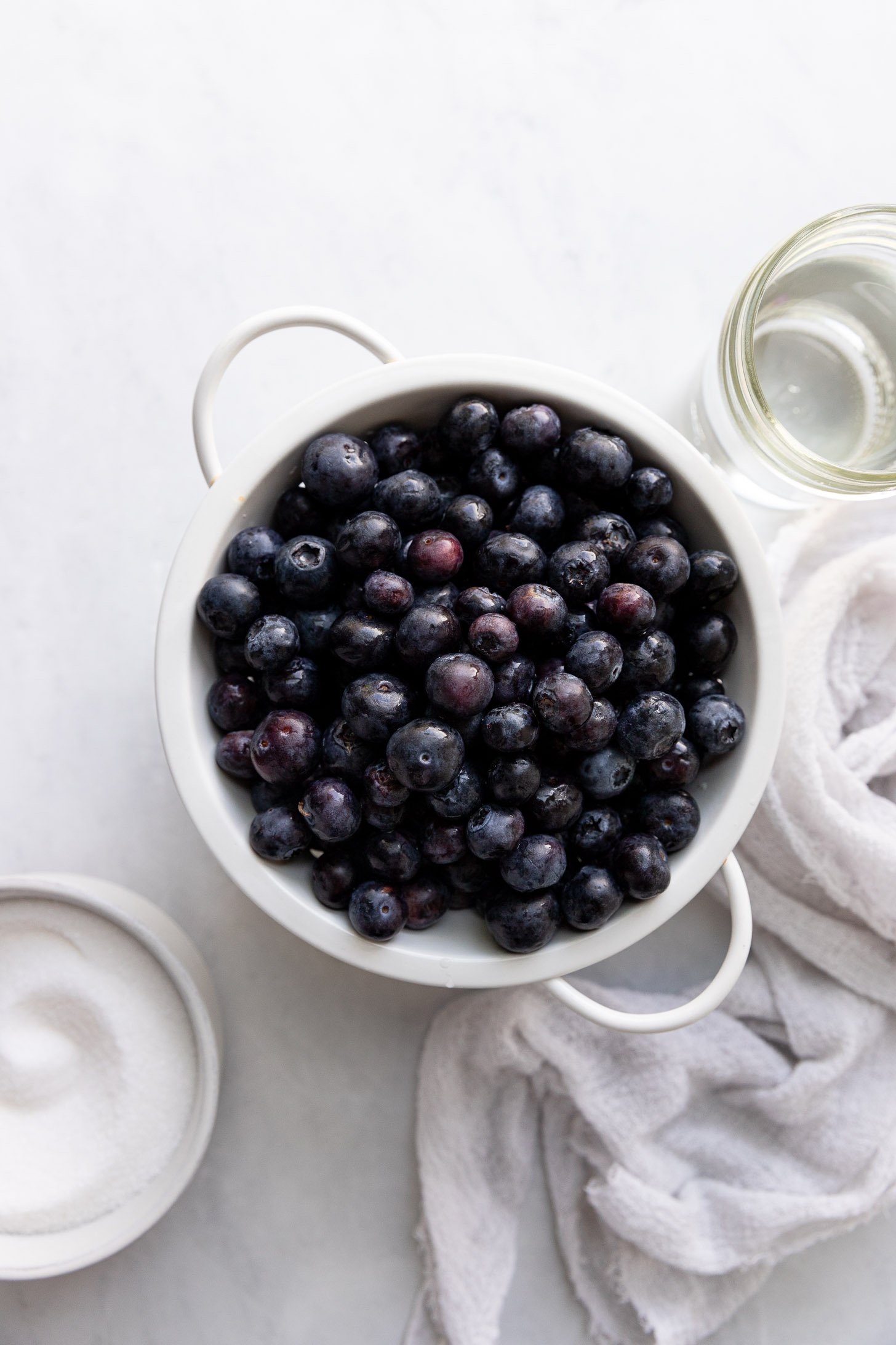 Strainer with blueberries and bowl of sugar.