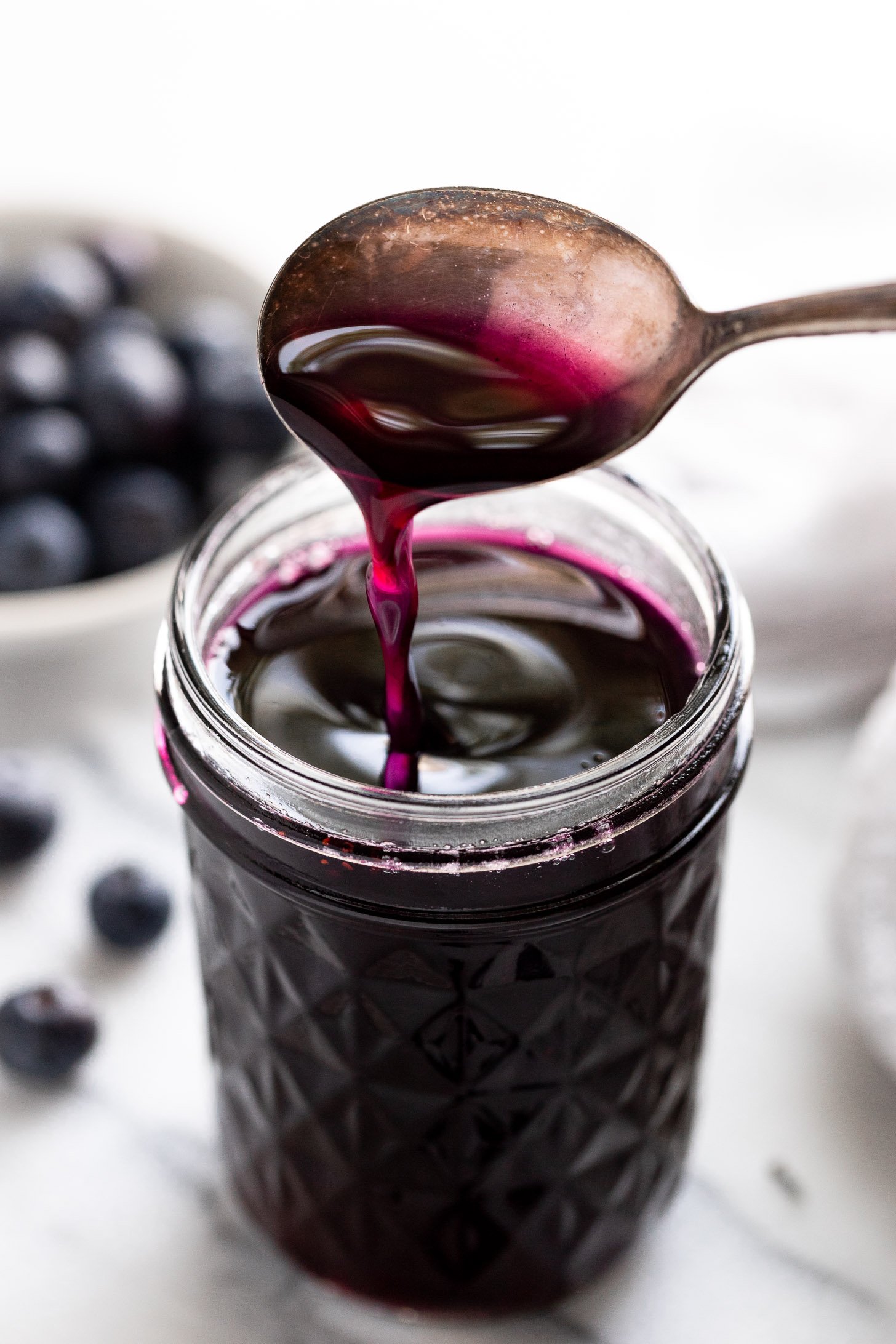 Spoon dripping blueberry syrup into jar.
