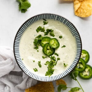 Bowl of creamy jalapeno sauce with pepper slices and cilantro.