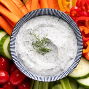 Creamy dill dip in bowl surrounded by chopped veggies.