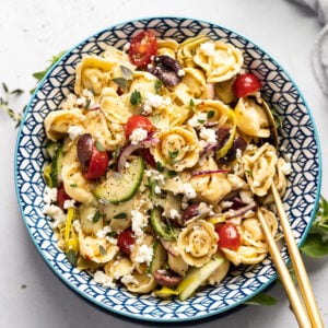 Bowl of greek tortellini salad with serving spoons.
