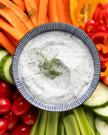 Creamy dill dip in bowl surrounded by chopped veggies.