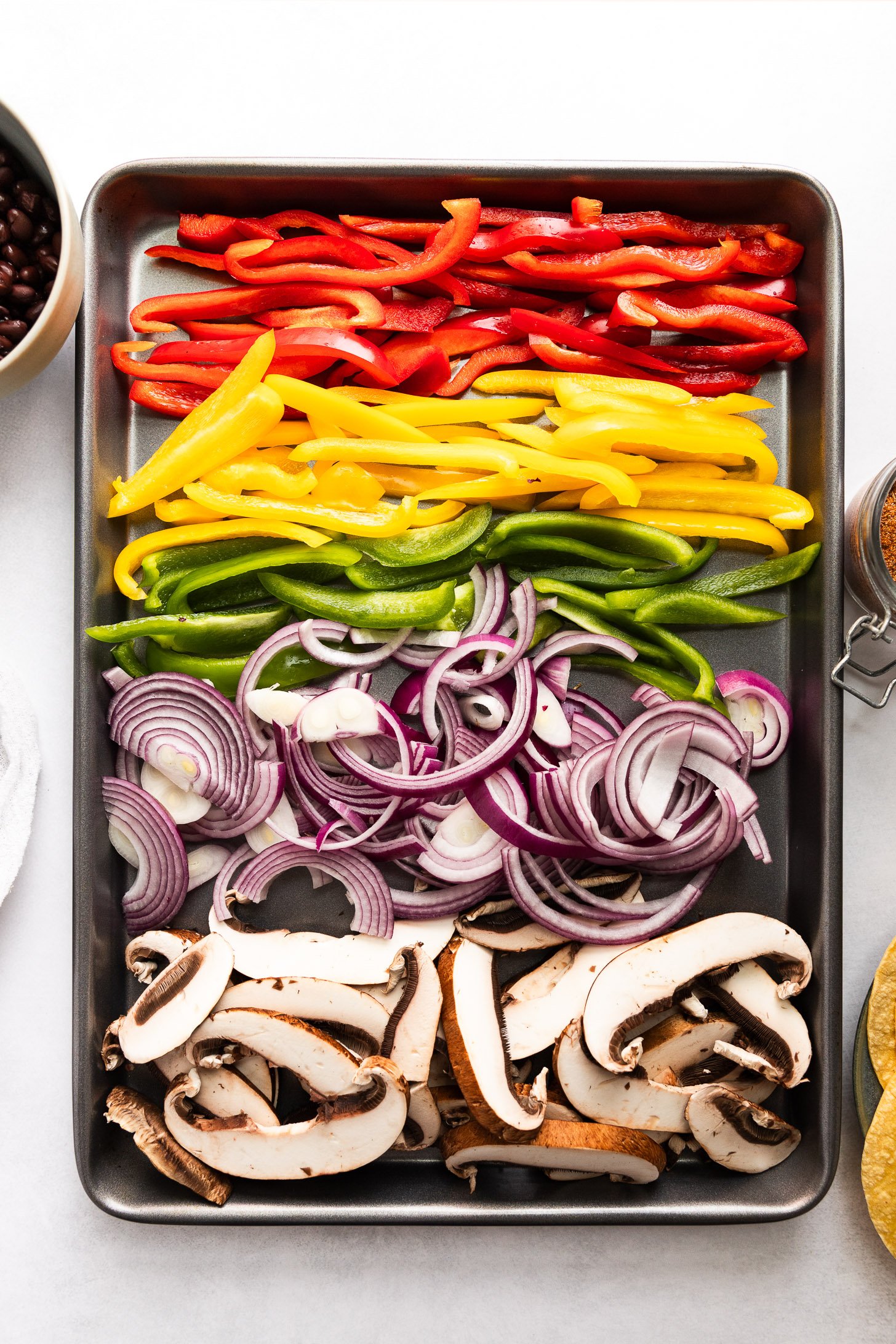Thinly sliced peppers, onion, and mushroom on sheet pan.