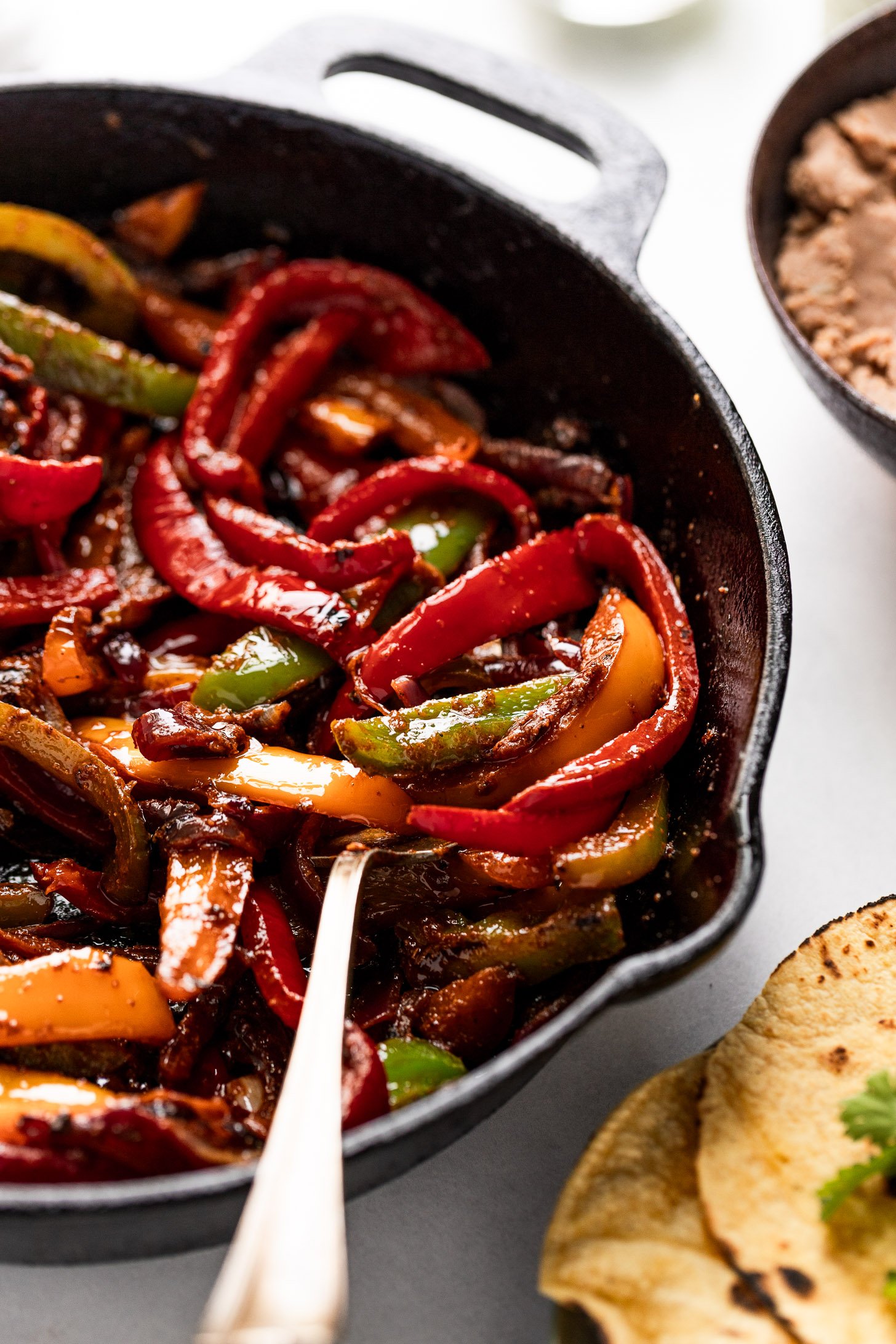 Fajita veggies in pan tossed with sauce with a serving spoon.