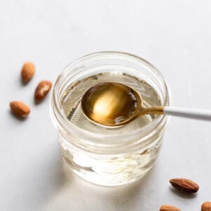 Jar of almond simple syrup with spoon scooping.