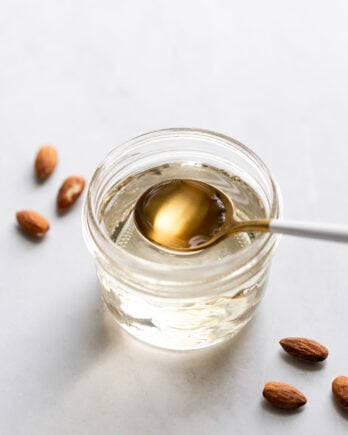 Jar of almond simple syrup with spoon scooping.