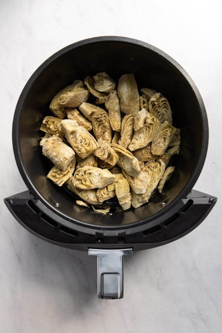 Air fryer basket with frozen artichoke hearts before cooking.